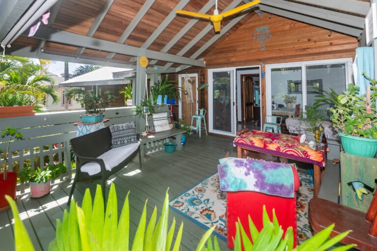 Colorful covered porch in Roatan with wooden ceiling, hanging decorations, potted plants, and outdoor seating arrangements overlooking neighboring houses and lush greenery in Honduras.