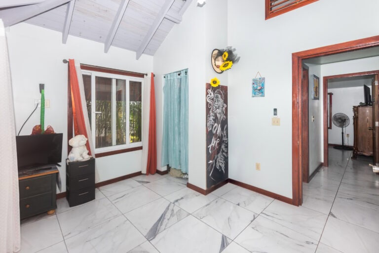Interior of a cozy living space in Roatan, Honduras, featuring white walls, colorful artwork, and a sliding glass door leading to a tropical outdoor area.