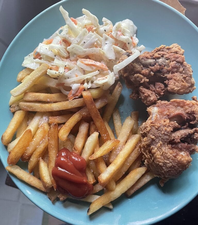 A plate of French fries topped with coleslaw, ketchup, and two pieces of fried chicken served on a blue plate in Roatan, Honduras.