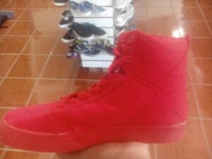 A person wearing red pants and red sneakers is standing on a terracotta-tiled floor next to a shoe rack with various pairs of shoes in Roatan, Honduras.