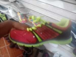 Colorful children's shoes are displayed on a white slat wall in a retail store on Roatan, Honduras.