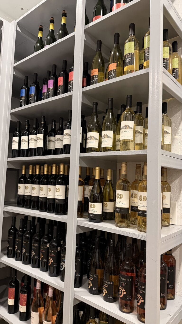 A display of various bottles of wine arranged on white wooden shelves inside a shop or restaurant in Roatan, Honduras.