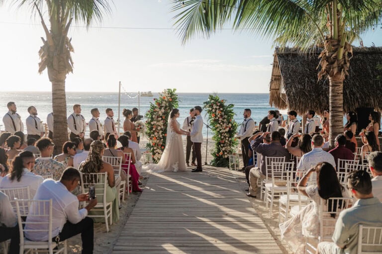 A beachfront wedding ceremony on Roatan, Bay Islands, Honduras, with a bride and groom exchanging vows under a decorated arch, surrounded by palm trees and sea views.