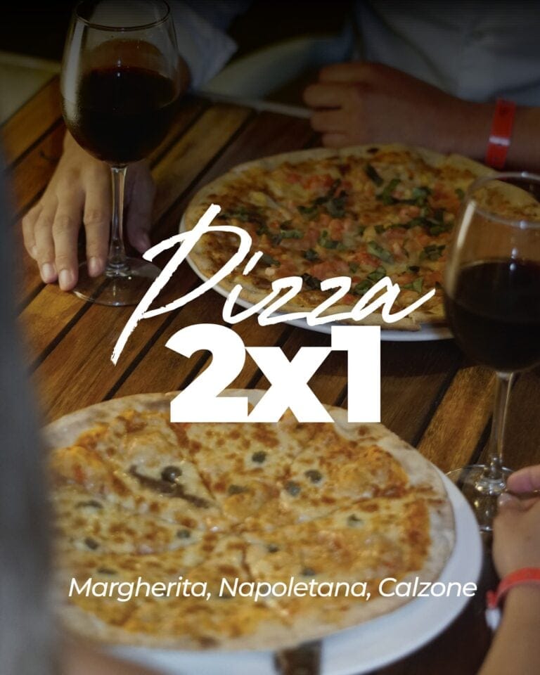 A person holding a glass of red wine next to a Margherita Neapolitan pizza topped with cheese, tomato sauce, and basil at a restaurant in Roatan, Honduras.