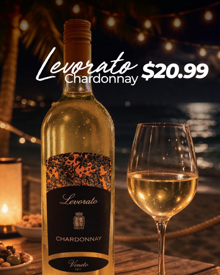 A bottle of Levorato Chardonnay wine and a filled wine glass are displayed on a wooden table at night with string lights and a thatched roof in the background, highlighting a tropical ambiance in Roatan, Honduras.