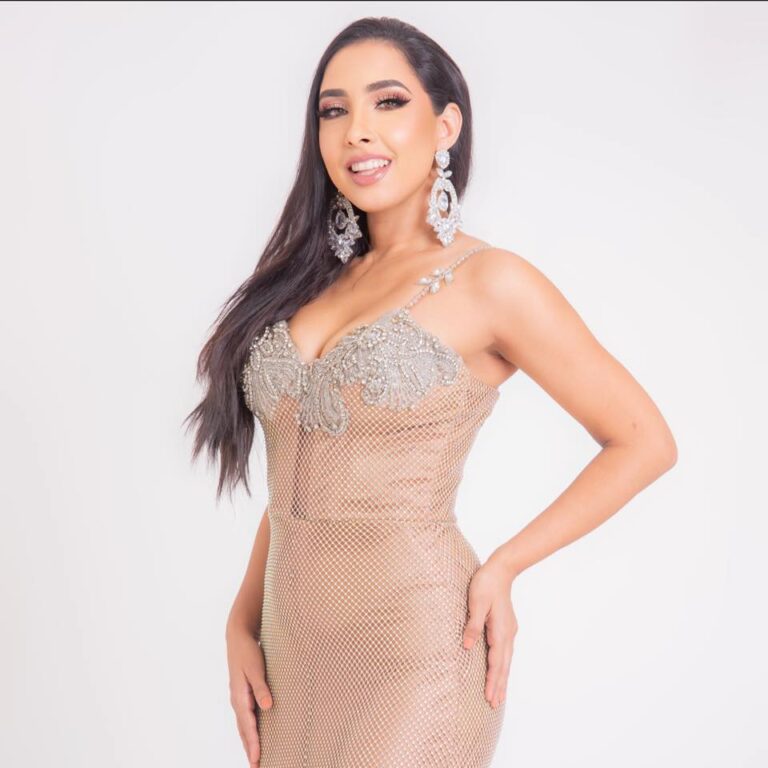 A woman in an elaborate, beaded gown and large jewelry poses confidently against a plain white background, showcasing glamorous attire perfect for a special occasion in Roatan, Honduras.