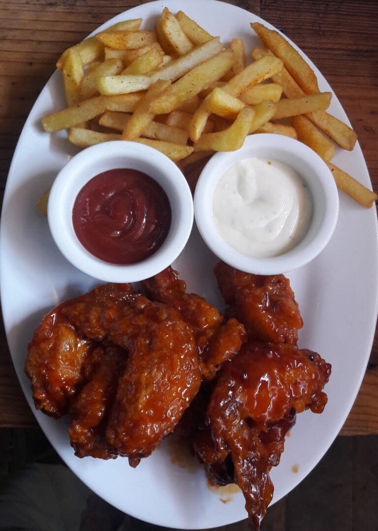 A plate of crispy French fries with two dipping sauces—ketchup and ranch—served on a white dish in a restaurant setting in Roatan, Honduras.