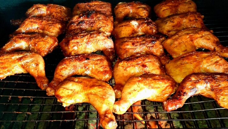 Grilled chicken pieces cooking on a barbecue grill in Roatan, Honduras, with a charred and glazed appearance.