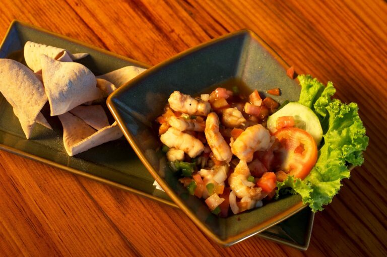A plate of traditional Honduran food with tortillas, a shrimp ceviche, and fresh vegetables served on a wooden table in Roatan, Honduras.