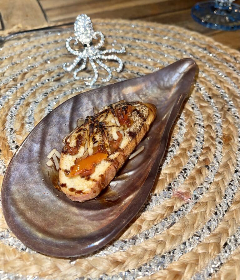 A grilled fish served on a metal plate with a bed of beans and a spicy sauce, set on a woven straw mat on a table in Roatan, Honduras.