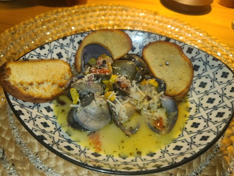 A bowl of Honduran-style seafood soup with clams, vegetables, and chopped herbs, served with toasted bread slices on a decorative black-and-white plate on a woven placemat in Roatan.