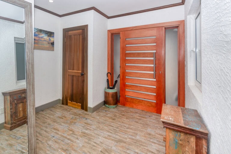 Interior view of a home in Roatan, Bay Islands, Honduras showcasing a wooden door, a small window, and rustic furniture with tropical design elements.