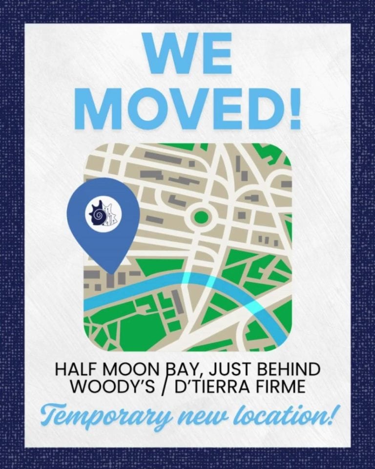 A colorful map with a blue location marker indicating a temporary new business location on Roatan, Honduras, featuring streets, green parks, a river, and the phrase "WE MOVED!" at the top.
