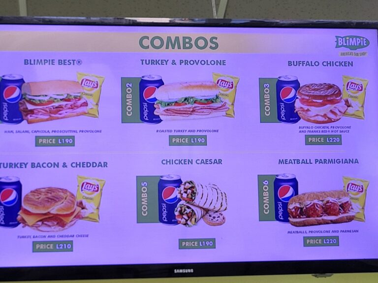A digital menu screen displaying various combo meal options at a restaurant in Roatan, Honduras, including items like turkey and provolone, buffalo chicken, and others, with images of sandwiches, snacks, and drinks.