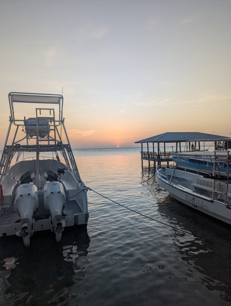 Boats docked at a pier on Roatan in Honduras during sunset, with calm water, a pavilion, and a clear sky in the background.