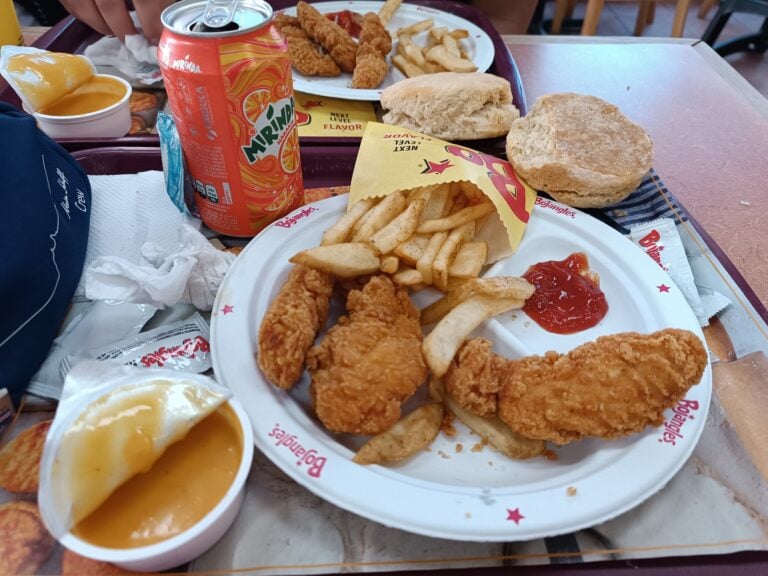 A tray of fried chicken tenders, French fries, bread rolls, dipping sauces, and a can of Mirinda orange soda is displayed on a table at a casual restaurant in Roatan, Honduras.