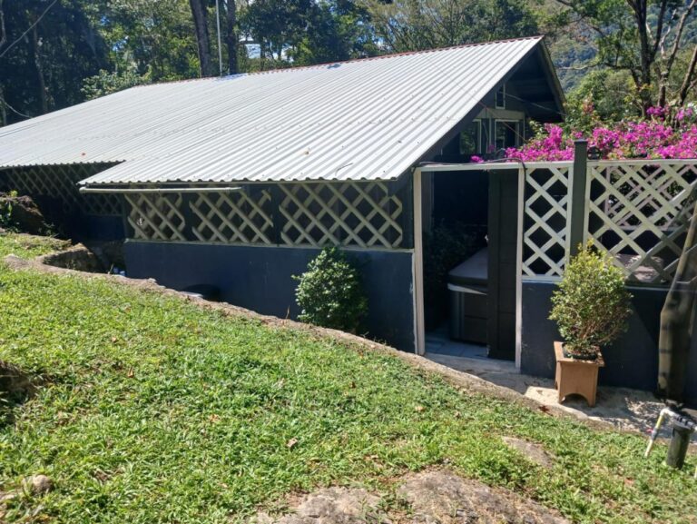 A small house with a corrugated metal roof and lattice fencing, surrounded by lush greenery and blooming pink flowers on Roatan, Honduras.