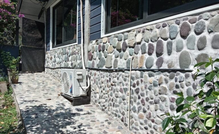 Section of a building in Roatan, Honduras, featuring a stone and wood exterior with large windows and an air conditioning unit outside.