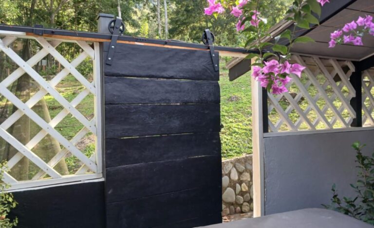 A black sliding gate made of wooden planks with decorative hardware, set against a white lattice fence and lush greenery, on Roatan Island in Honduras.
