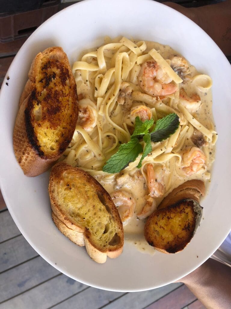 A plate of shrimp Alfredo pasta garnished with fresh mint leaves and served with toasted bread slices on the side, set on a wooden surface in Roatan, Honduras.