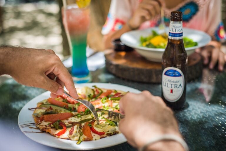 People enjoying a meal with a slice of pizza and drinks at an outdoor dining area in Roatan, Honduras.