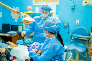 Dental professionals wearing protective gear perform an oral procedure in a brightly colored dental clinic on Roatan, Honduras.
