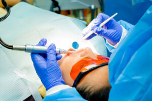 A medical professional wearing blue gloves performs a dental procedure on a patient lying down with an orange protective bib in a clinic in Roatan, Honduras.