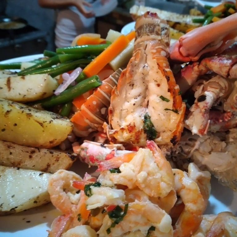 A seafood platter featuring lobster, shrimp, grilled fish, and assorted vegetables served on a plate in Roatan, Honduras.