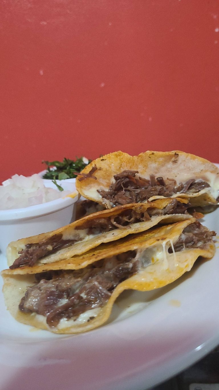 Stacked beef tacos filled with shredded meat, served on a white plate with a small side of chopped onions and cilantro in the background, highlighting local cuisine in Roatan, Honduras.