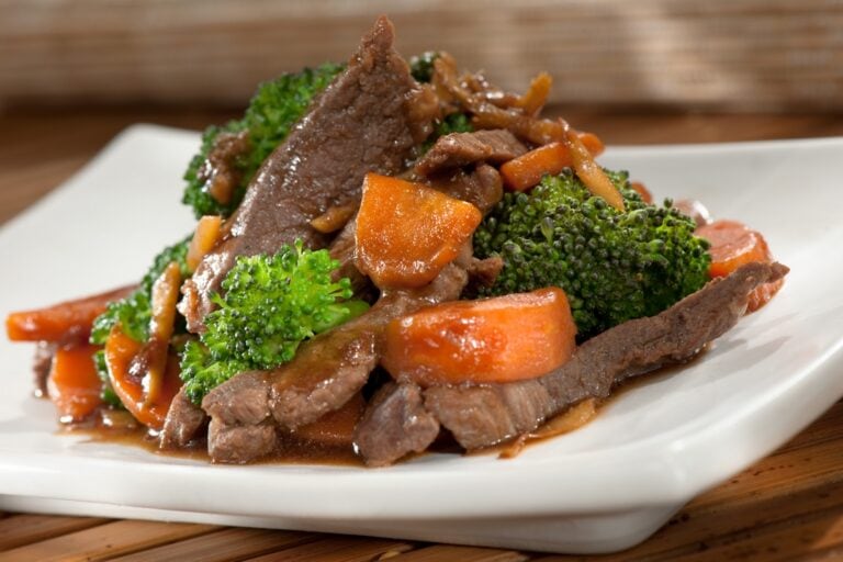 A plate of beef stew with broccoli and carrots served on a white dish, with a wooden background, showcasing Honduran cuisine in Roatan, Honduras.