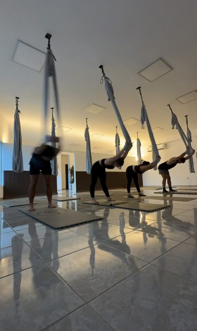 People practicing aerial yoga using hammock equipment in a spacious indoor studio on Roatan, Honduras.