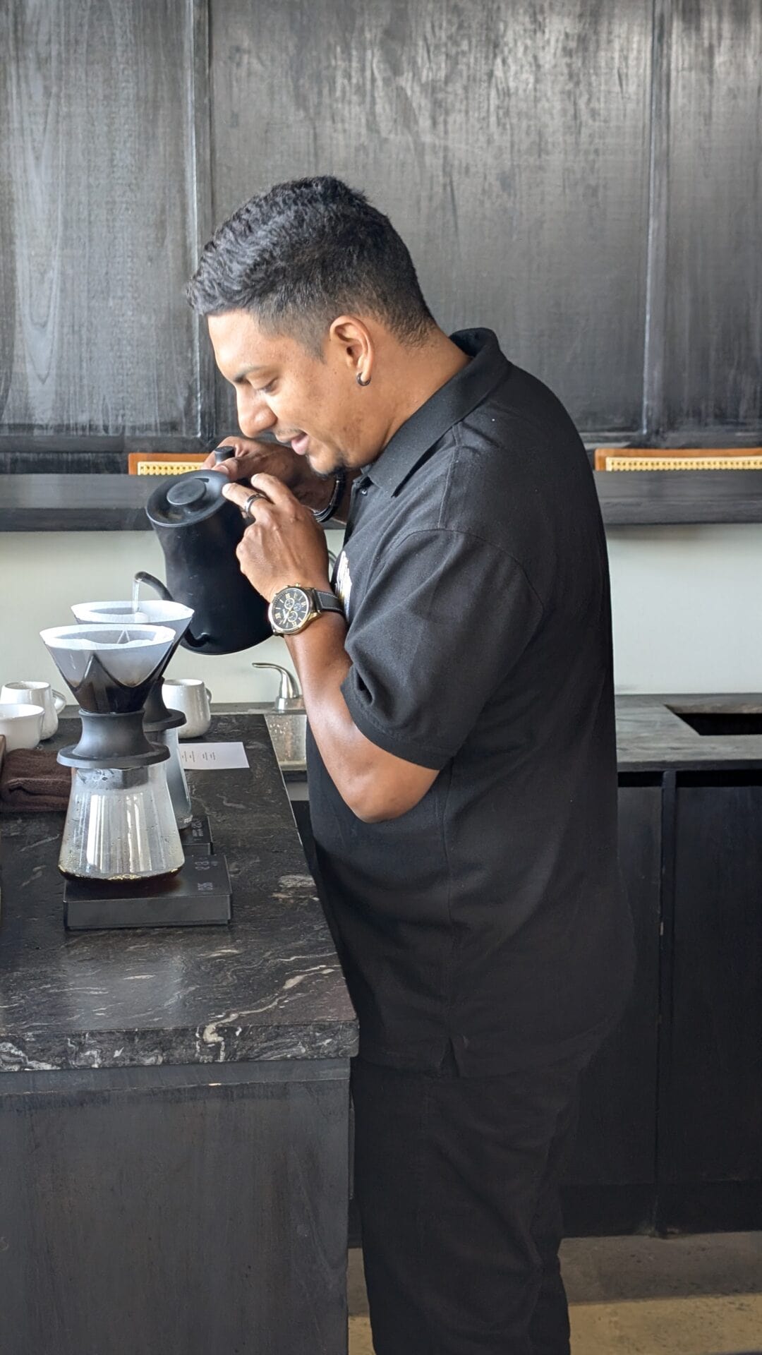 Young barista on Roatan, Honduras, preparing pour-over coffee at a modern coffee shop.