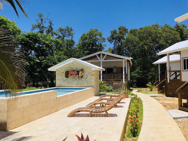 A resort swimming pool area with several lounge chairs, a small building with a "Coach Gasitas" sign, surrounded by lush greenery and tall trees in Roatan, Honduras.
