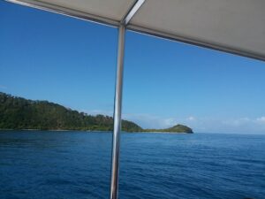 A view of the ocean with a distant green island on the horizon, taken from a boat in Roatan, Honduras, with part of a beige canopy and metal frame visible in the upper portion of the image.