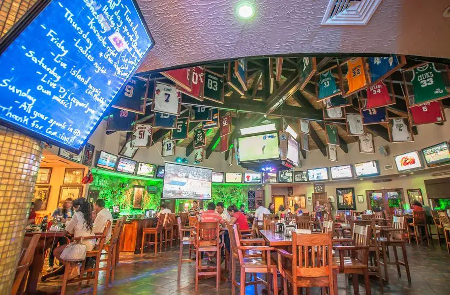 Interior of Herby’s Sports Bar & Grill in French Harbour with suspended jerseys, multiple TVs, and a central scoreboard