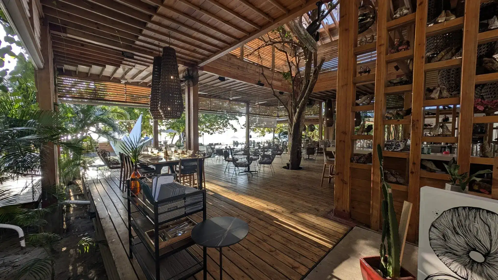 Inside a rustic yet elegant open-air restaurant or bar in Roatan, Honduras, featuring wooden beams, a tree growing through the space, and ample seating with tables and chairs overlooking a view of the ocean.