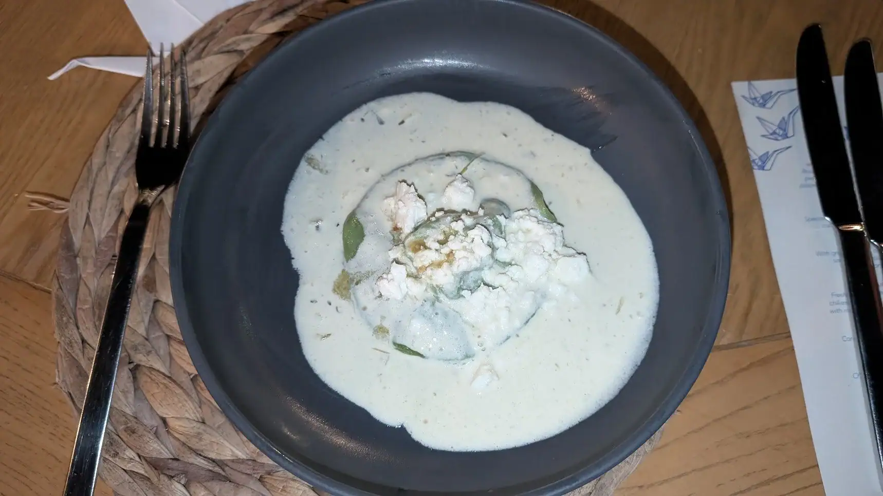 A bowl of creamy white Honduran seafood dish served on a dark plate, garnished with herbs, placed on a woven placemat on a wooden table in Roatan, Honduras.