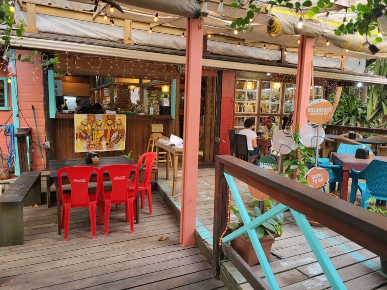 A colorful outdoor dining area in Roatan, Honduras, features wooden decking, vibrant chairs, string lights, and a covered seating space with tropical decor.