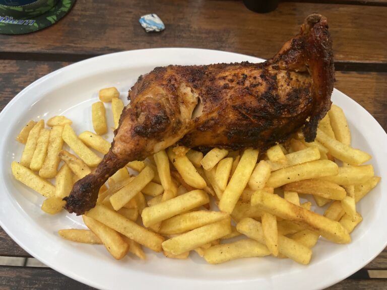 A plate of crispy French fries topped with a grilled chicken leg served on a white dish in a restaurant on Roatan, Honduras.