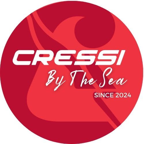 The Cressi by the Sea logo featuring a stylized red wave and surfboard design, with the text 'Cressi By The Sea Since 2024' on a circular red background, representing a water sports company in Roatan, Honduras.