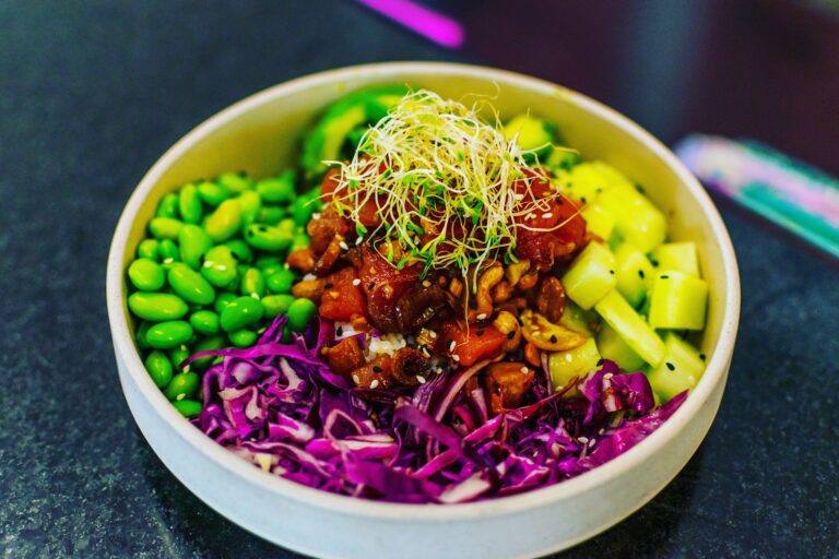 A vibrant acai bowl with mixed vegetables, sprouts, purple cabbage, and sesame seeds is shown in a white bowl on a dark countertop, representing healthy food options available in Roatan, Honduras.