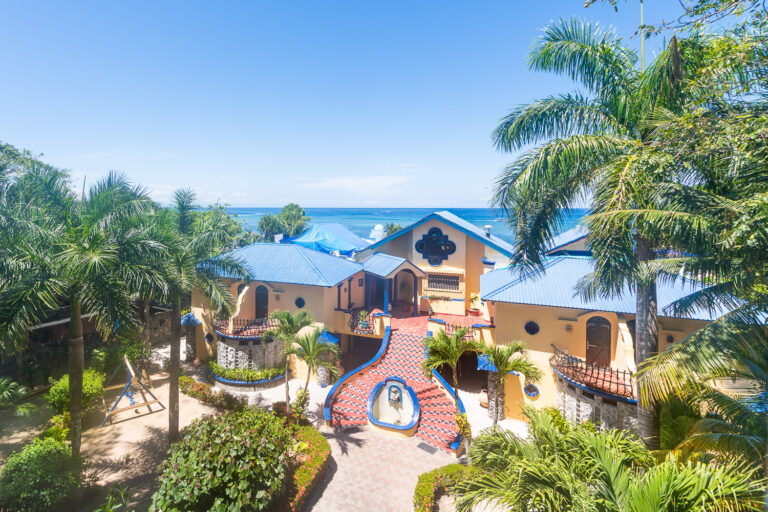 Colorful tropical villa with blue rooftops surrounded by lush palm trees overlooking the Caribbean Sea in Roatan, Honduras.