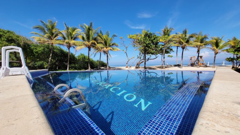 A swimming pool with blue tiles reflecting palm trees and the Caribbean Sea near Roatan in Honduras, surrounded by lush greenery and clear blue skies.
