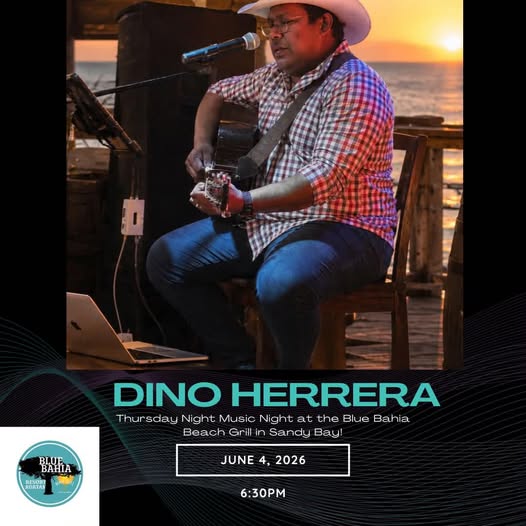 A musician wearing a checkered shirt and a cowboy hat plays an acoustic guitar while singing into a microphone at a sunset outdoor venue on Roatan, Honduras.
