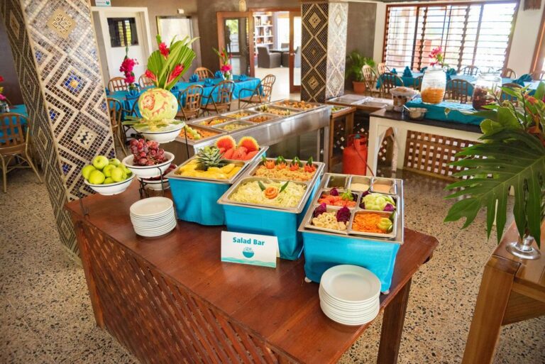 Fresh fruit and salad ingredients at a salad bar in a tropical restaurant setting on Roatan, Honduras with colorful floral decorations and large windows.