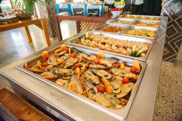 A variety of seafood dishes, including mussels and shrimp, served in stainless steel trays at a buffet in Roatan, Honduras.
