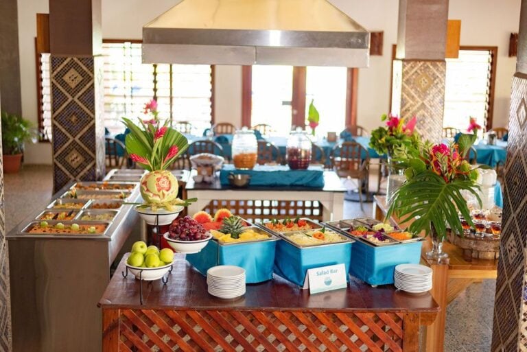 Buffet setup at a restaurant in Roatan, Honduras, featuring a variety of tropical fruits, salads, and decorative flower arrangements with lush greenery in the background.