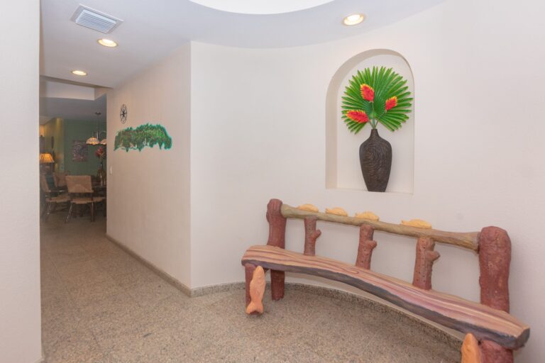 A crafted wooden bench with a unique rustic design, situated against a white wall in a cozy interior space on Roatan, Honduras, decorated with tropical-inspired art and accessories.