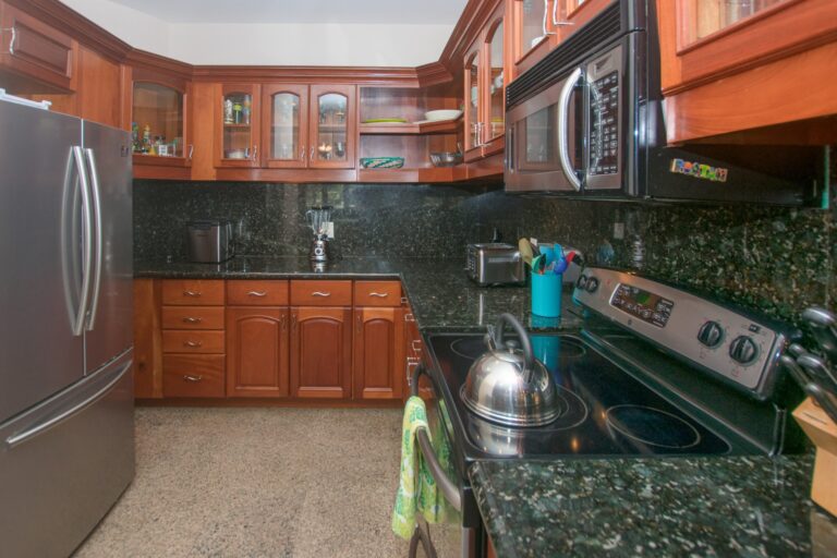 Wooden kitchen cabinets with glass doors and black granite countertops in a home on Roatan, Honduras.
