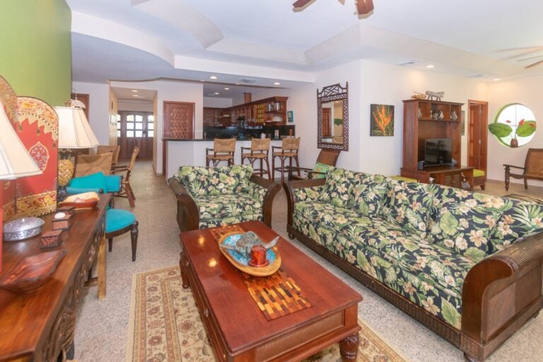 Spacious living room in a Caribbean-style house on Roatan, Honduras, featuring floral-patterned sofas, wooden furniture, decorative artwork, and tropical accents.